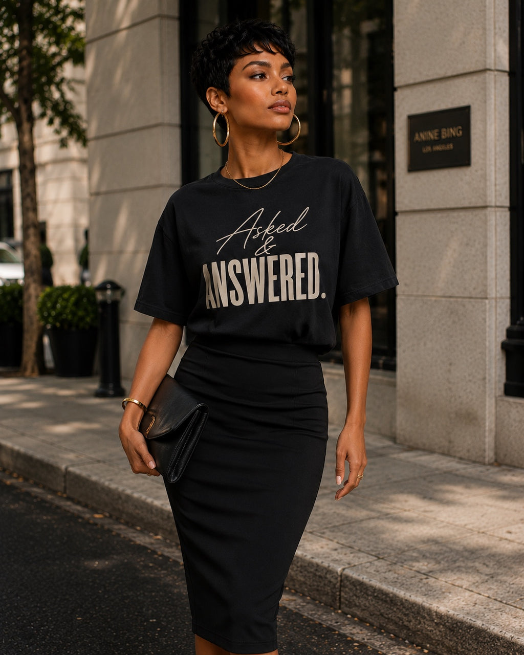 Woman wearing the Asked & Answered black statement tee with a black pencil skirt, clutch, and oversized gold hoops.