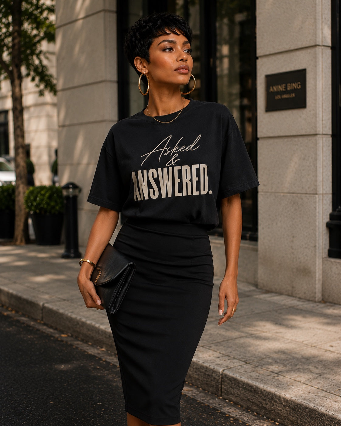 Woman wearing the Asked & Answered black statement tee with a black pencil skirt, clutch, and oversized gold hoops.