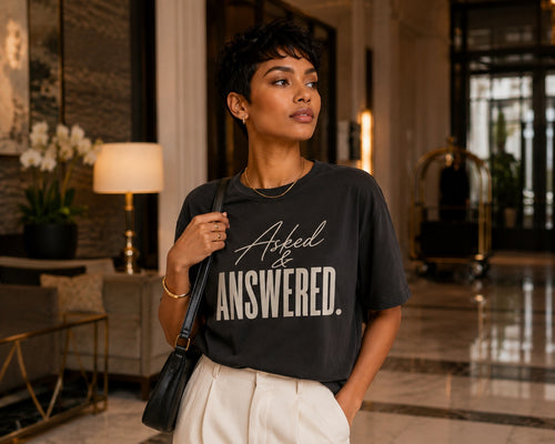 Woman wearing the Asked & Answered statement tee in Comfort Colors Pepper inside a luxury hotel lobby.