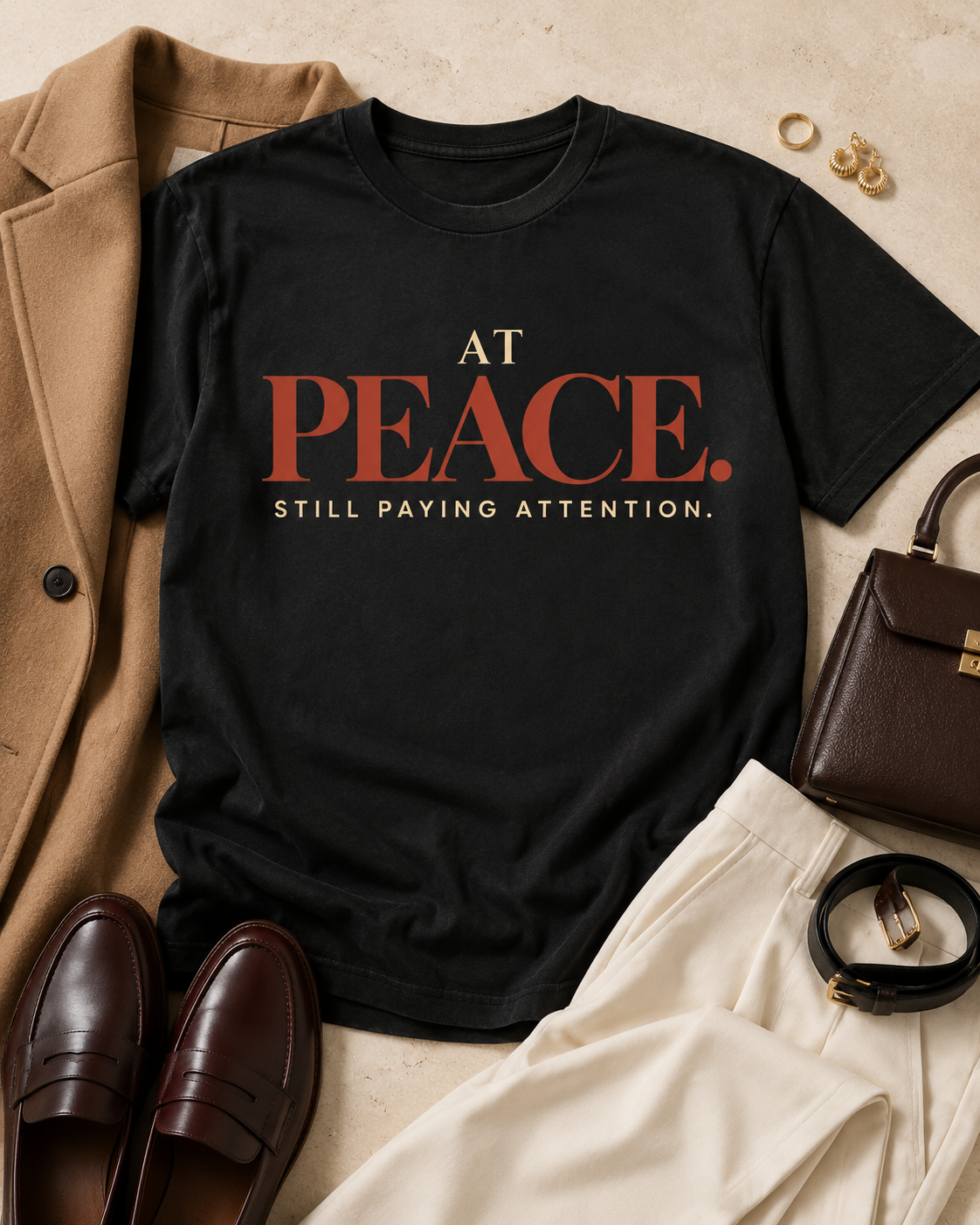 Styled flat lay of the At Peace Still Paying Attention Comfort Colors Black statement tee with a camel blazer, cream trousers, brown loafers, and gold jewelry.
