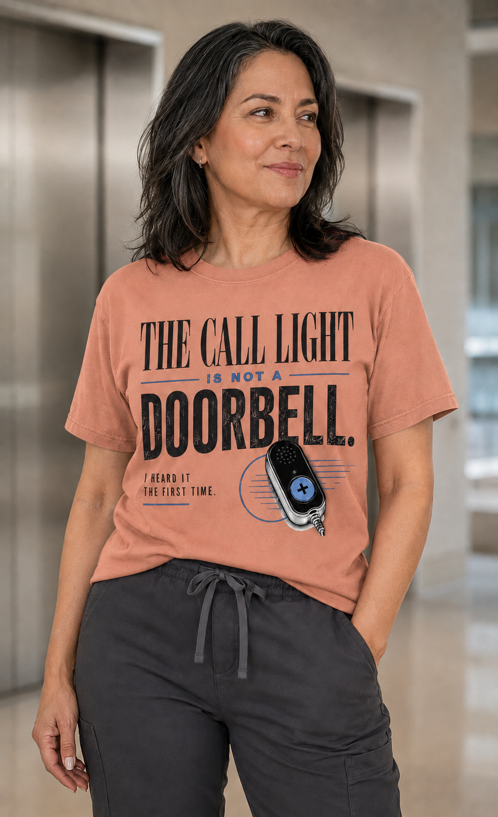 Hispanic nurse wearing Comfort Colors Terracotta Call Light Is Not a Doorbell tee with charcoal scrub pants