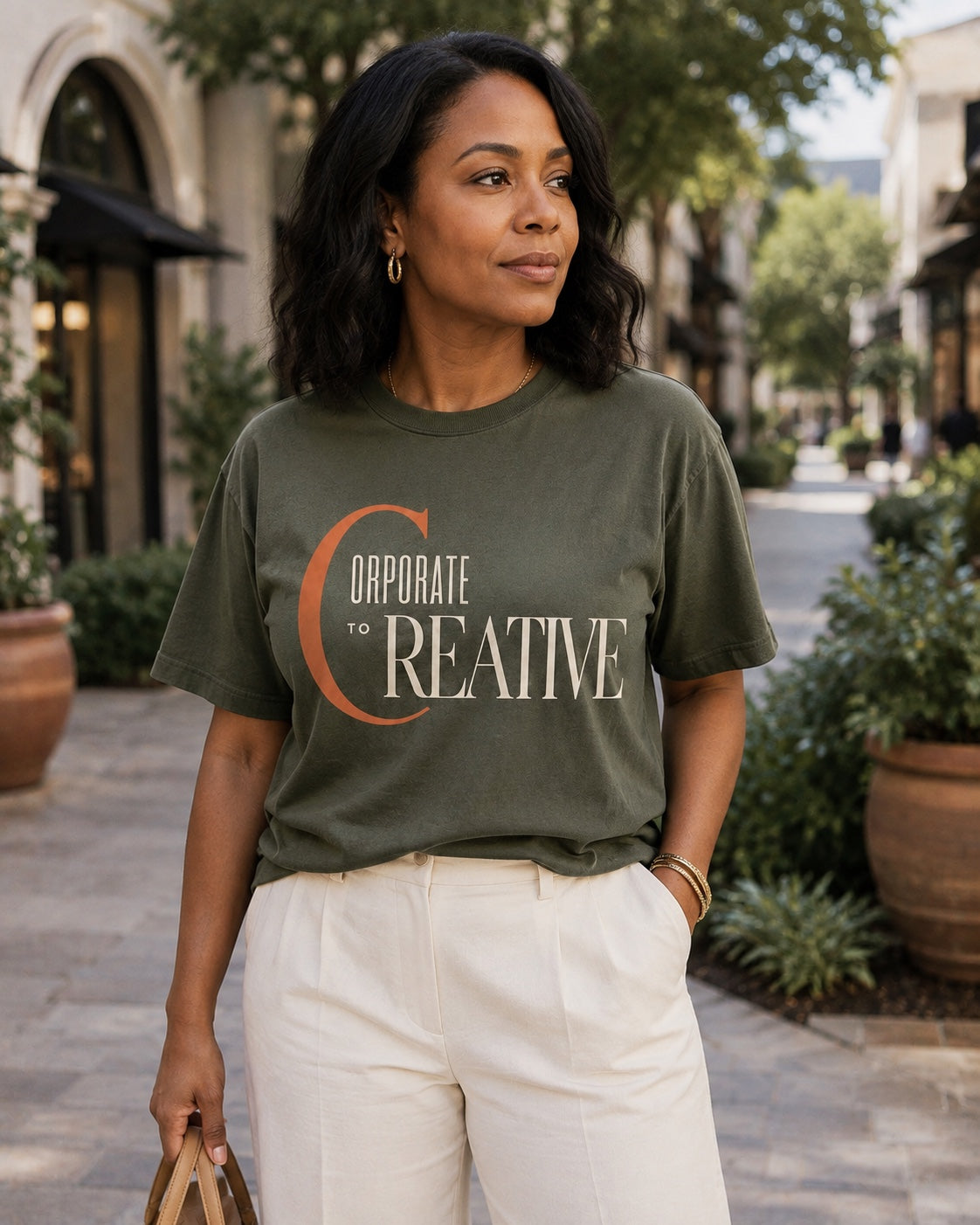 Woman wearing the Corporate to Creative statement tee in Comfort Colors Moss in an open-air shopping district