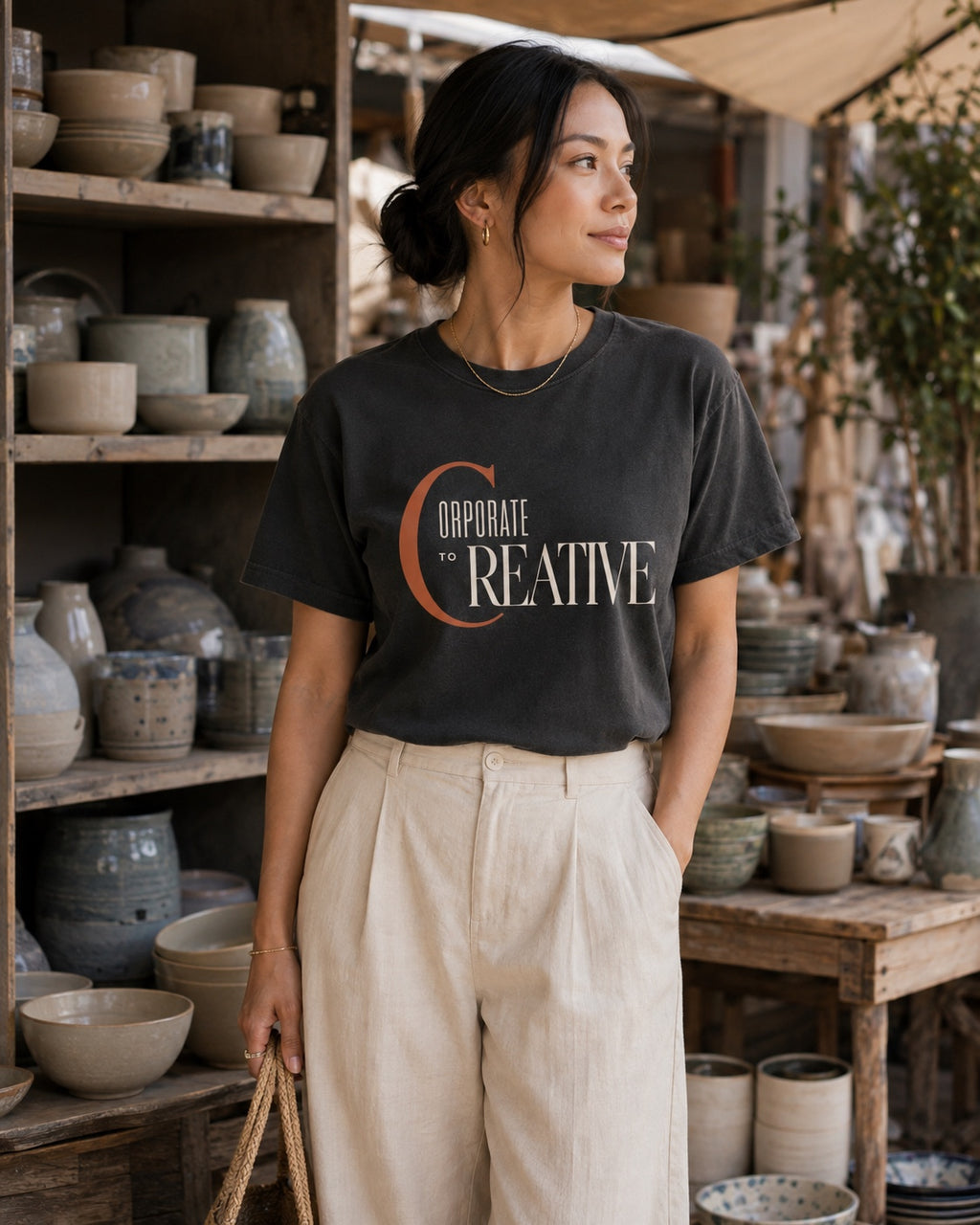 Woman wearing the Corporate to Creative statement tee in Comfort Colors Pepper while browsing handmade pottery