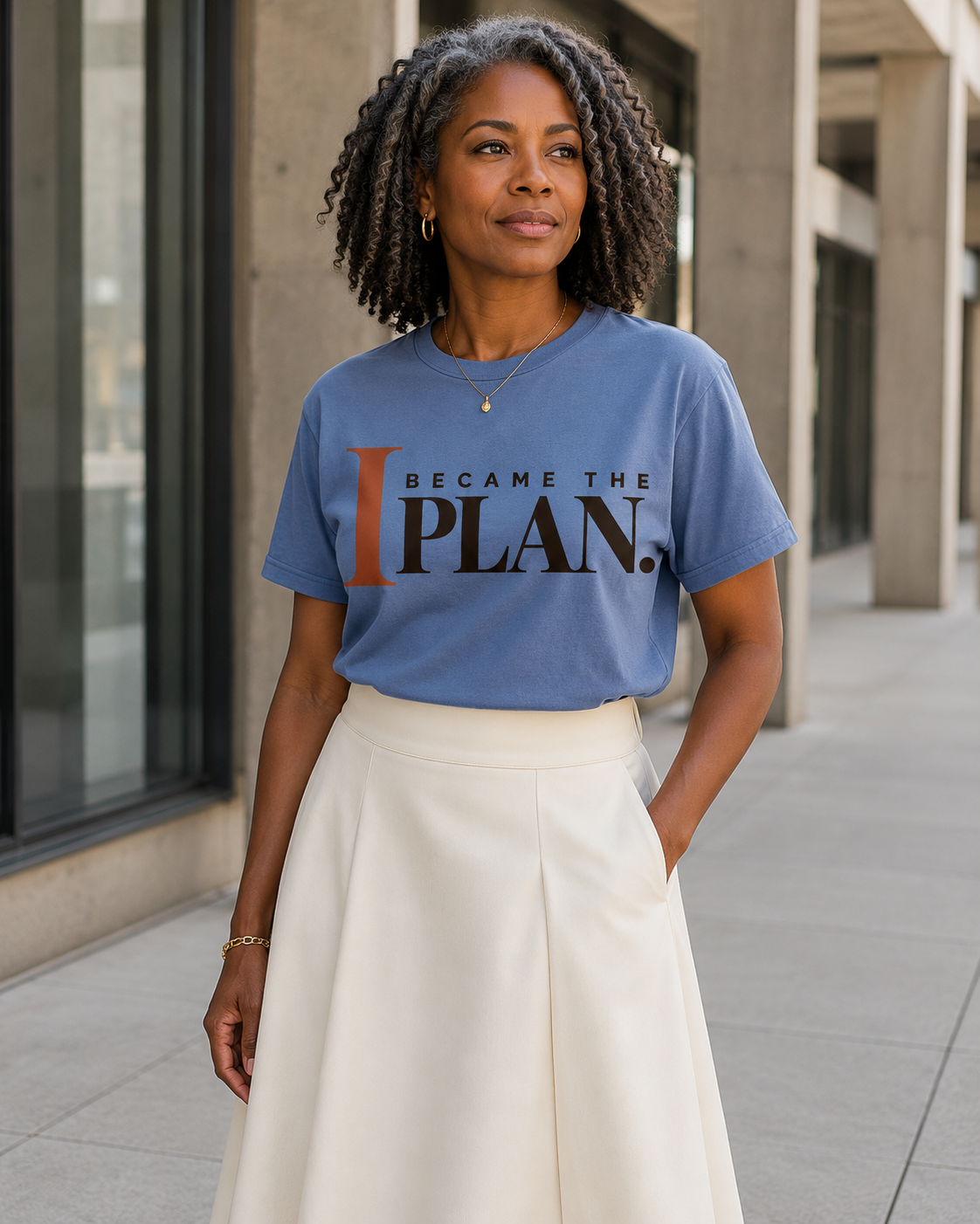 African American woman wearing the I Became the Plan statement tee in blue jean with an ivory midi skirt