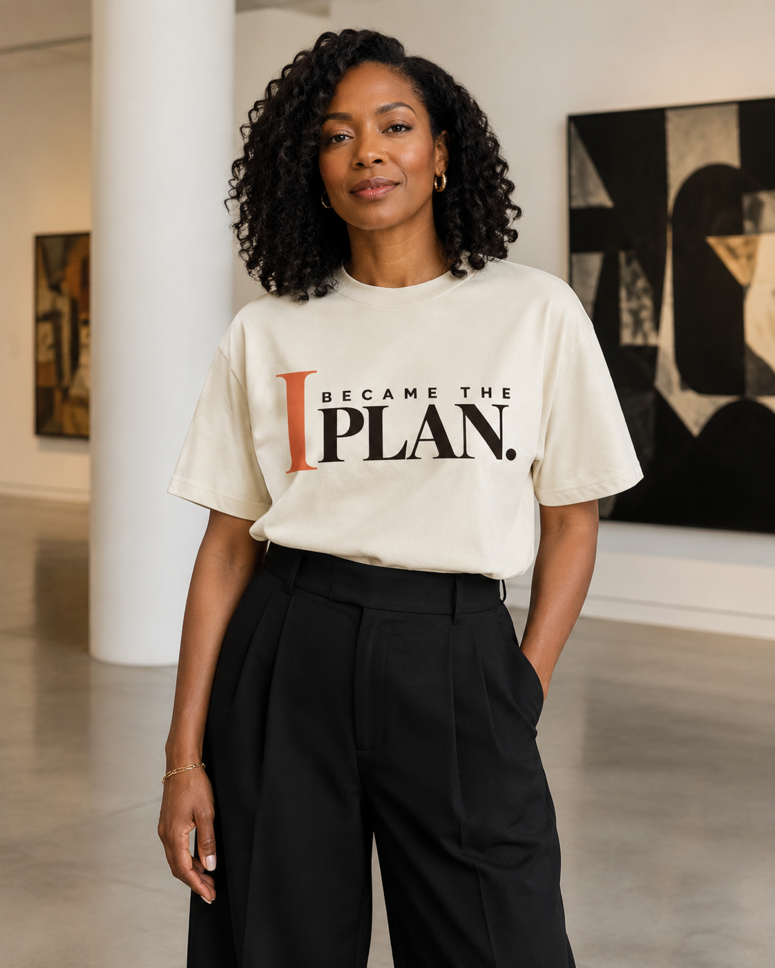 African American woman wearing the I Became the Plan statement tee in ivory with black tailored trousers