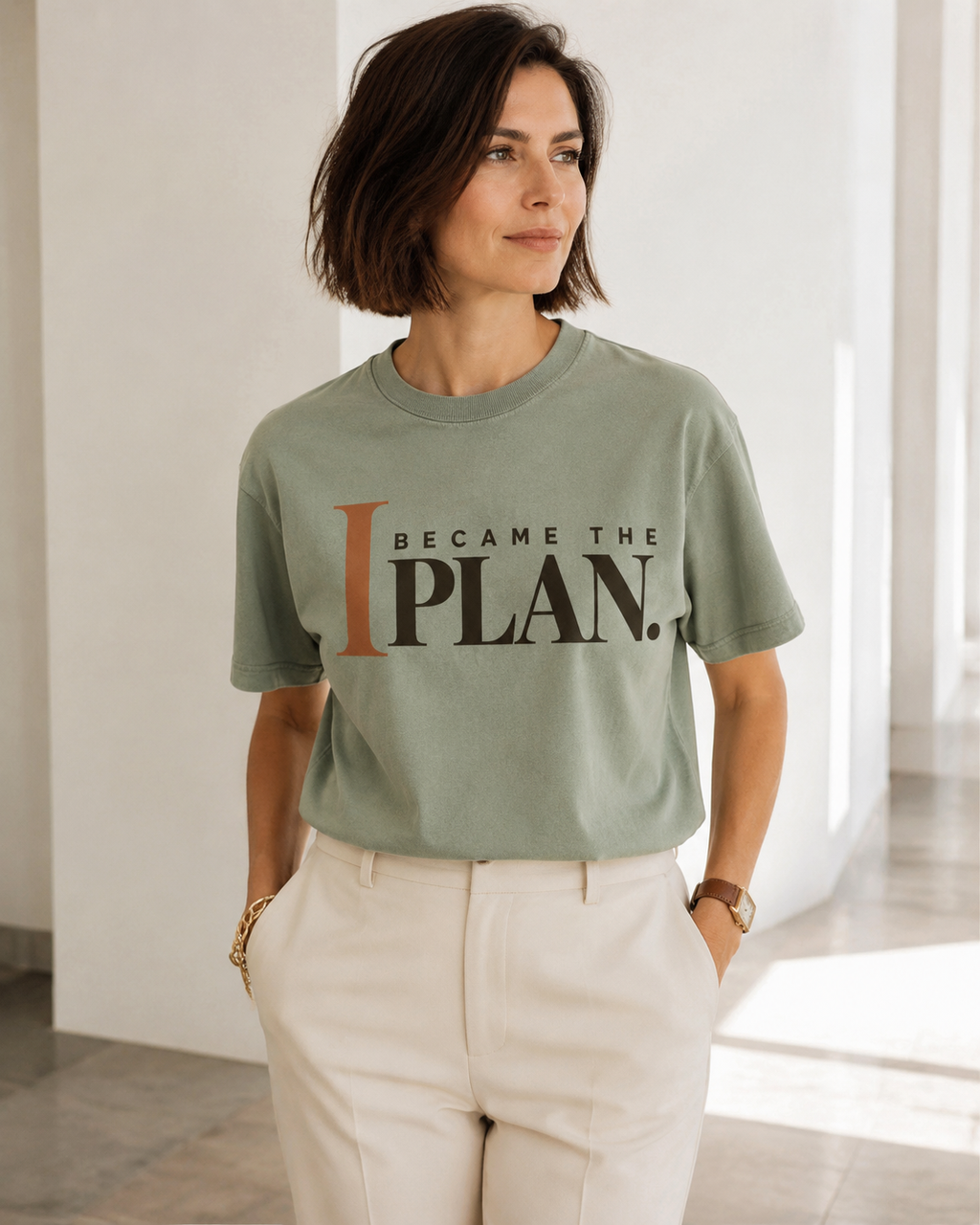Woman wearing the I Became the Plan statement tee in sage with cream tailored trousers