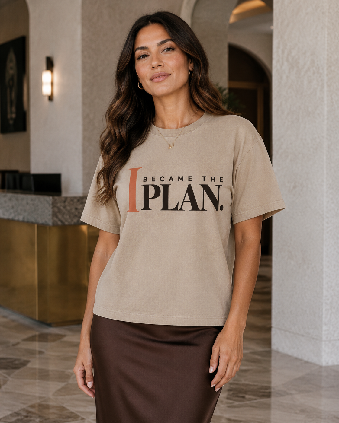 Hispanic woman wearing the I Became the Plan statement tee in sandstone with a chocolate midi skirt