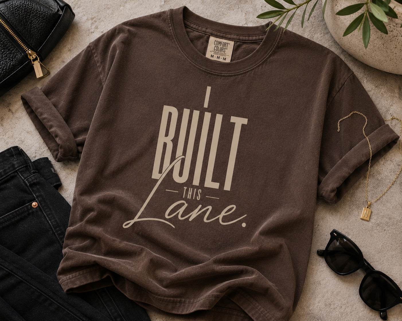 I Built This Lane espresso statement tee flat lay with black denim and gold accessories