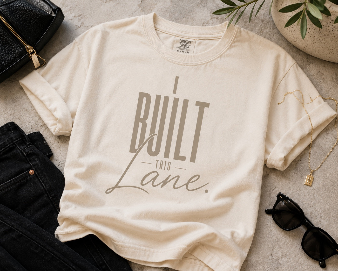 I Built This Lane ivory statement tee flat lay with black denim and gold accessories