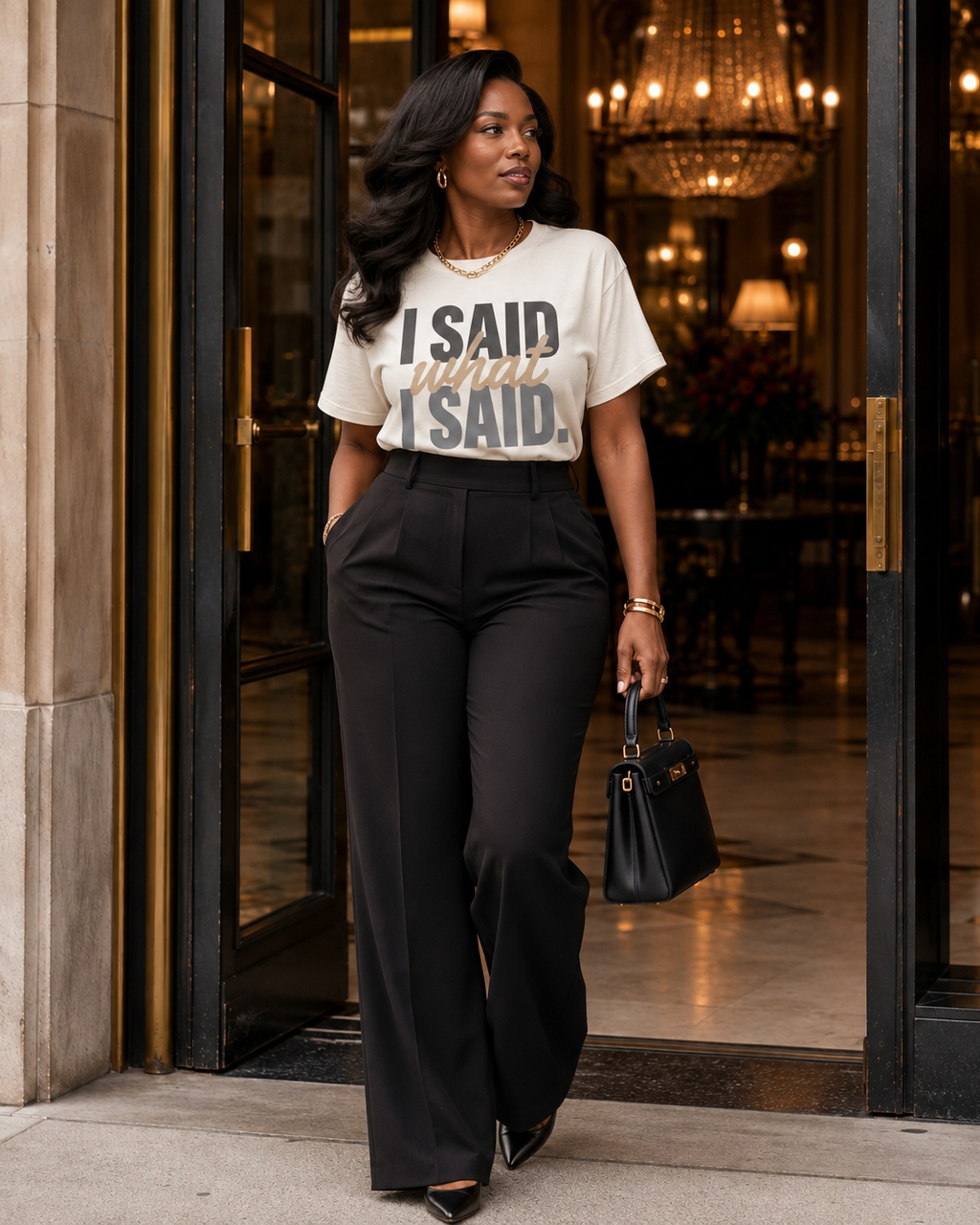 Woman wearing the I Said What I Said statement tee in Comfort Colors Ivory styled with black high-waisted tailored trousers at an upscale hotel entrance.