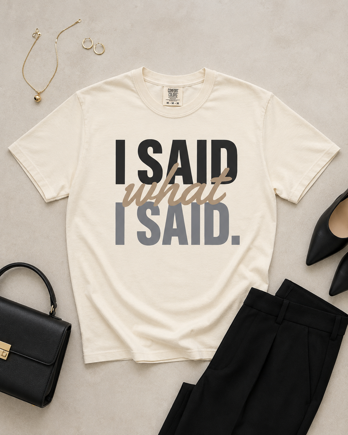 Styled flat lay of the I Said What I Said Comfort Colors Ivory statement tee with black tailored trousers, handbag, heels, and gold jewelry.