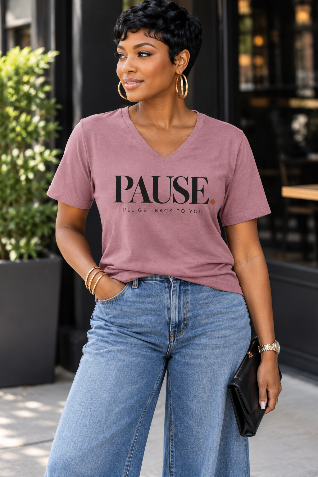 Woman wearing the PAUSE. I'll Get Back to You. women's V-neck statement tee in Mauve with wide-leg light-wash denim, gold hoops, and a black clutch