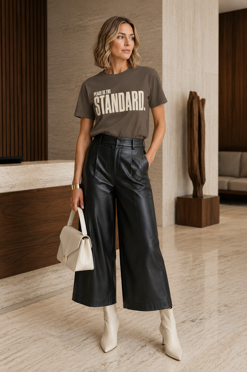 Woman wearing the Peace Is the Standard Comfort Colors Espresso statement tee with black leather culottes and ivory accessories.