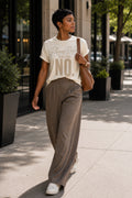 Woman walking in the Please Refer to My Last No. Comfort Colors Ivory tee with wide-leg trousers and white sneakers.