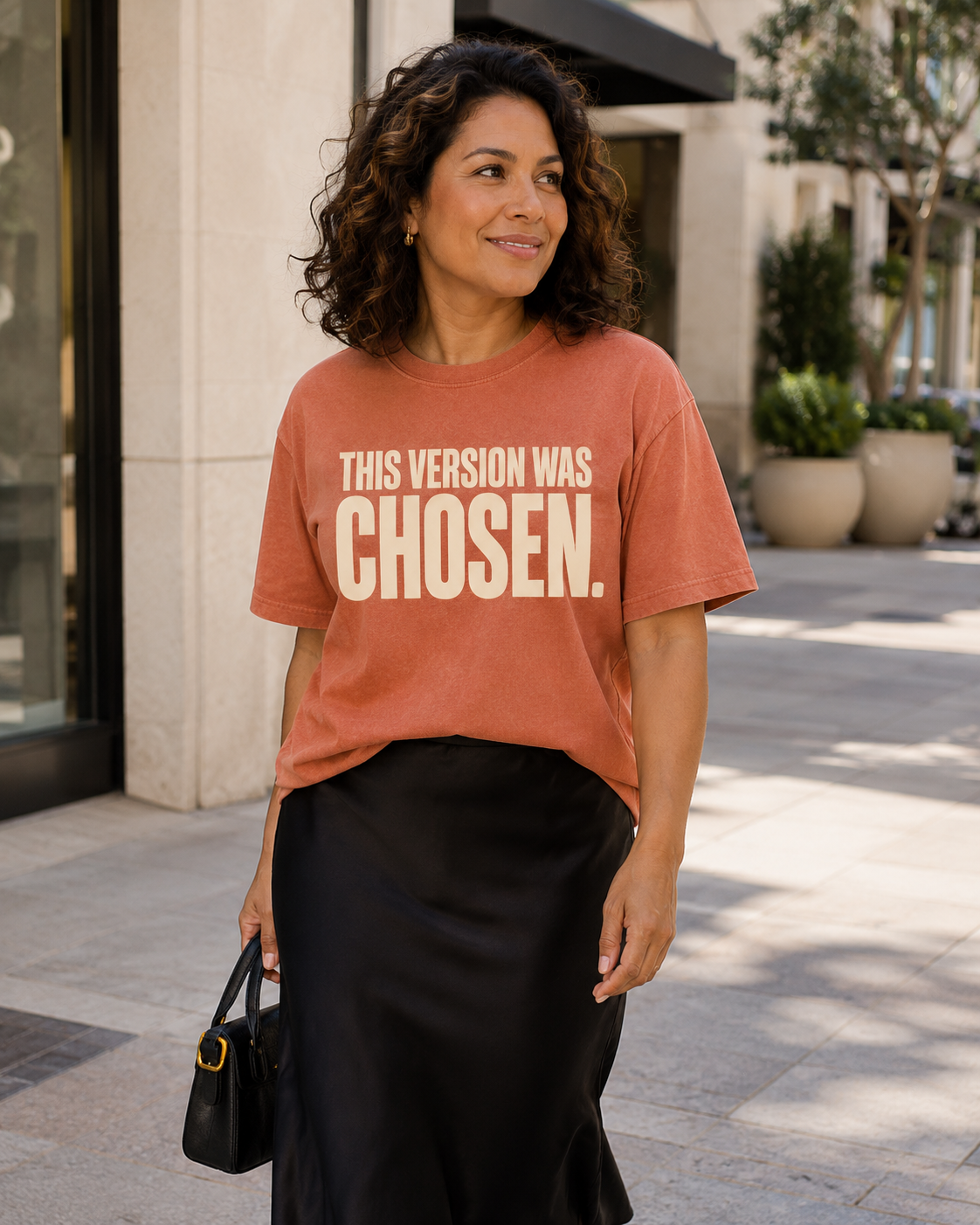 Hispanic woman wearing the This Version Was Chosen statement tee in terracotta with cream typography